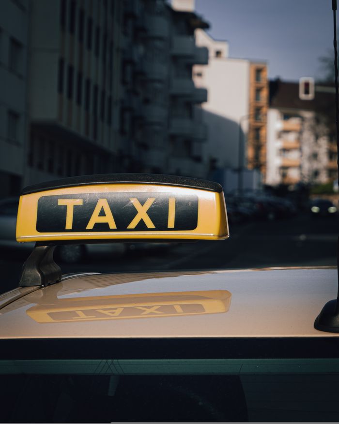 gallery-6 Close-up of a taxi sign on a car roof with an urban city background.