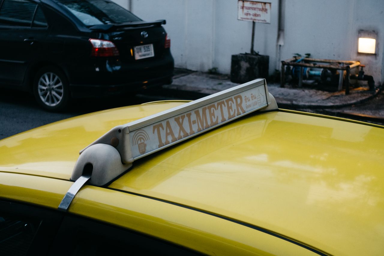 about-img Close-up of a yellow taxi's roof with a taxi meter sign in an urban environment.
