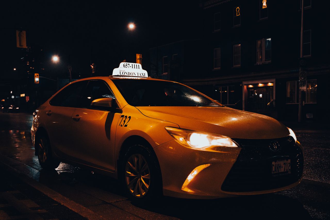 hero-img-02 A yellow taxi waiting at night in London, Ontario, Canada. Urban transportation captured with street lights.