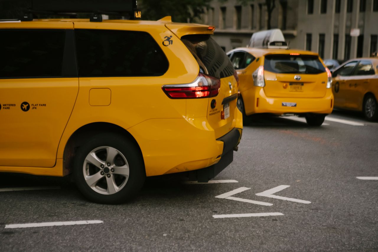 gallery-2 Modern yellow crossover taxi cars riding on asphalt road near commercial buildings in city