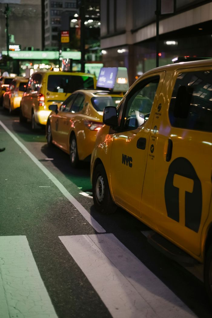 services-img Row of modern various yellow taxi vehicles parked on city street near buildings in New York at night
