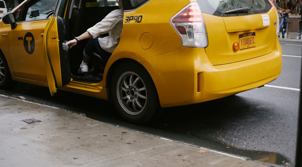 services-03 Unrecognizable passenger closing door of yellow cab with logo and headlight parked on asphalt road near pavement on street in city
